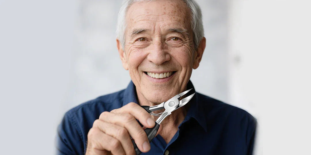Smiling elderly man holding precision nail clippers close to his face, neutral background.
